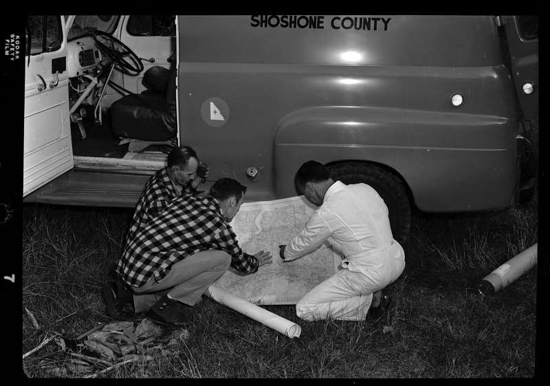 Three men from Shoshone County Search and Rescue crouched next to the vehicle while looking at a map.