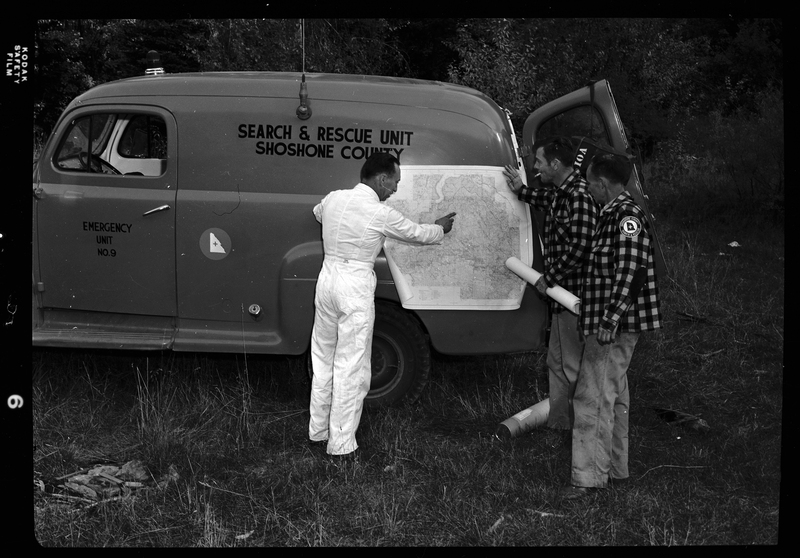 Three men from Shoshone County Search and Rescue standing next to the vehicle while looking at a map that is held up against the vehicle. The car is emergency unit number 9.