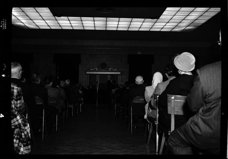 View of Gyro Club's anti-communism meeting from the back of the crowd, looking up the aisle to the panel of speakers.