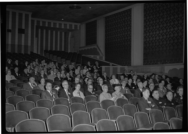 Crowd of unidentified men and women attending the Rotary international Club Convention. They are seating in rows in what might be a theatre or auditorium.