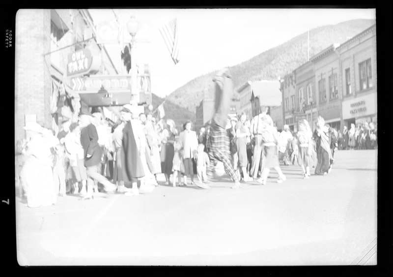 There is a person mid flip during the Benevolent and Protective Order of Elks parade. People and buildings can be seen in the background.