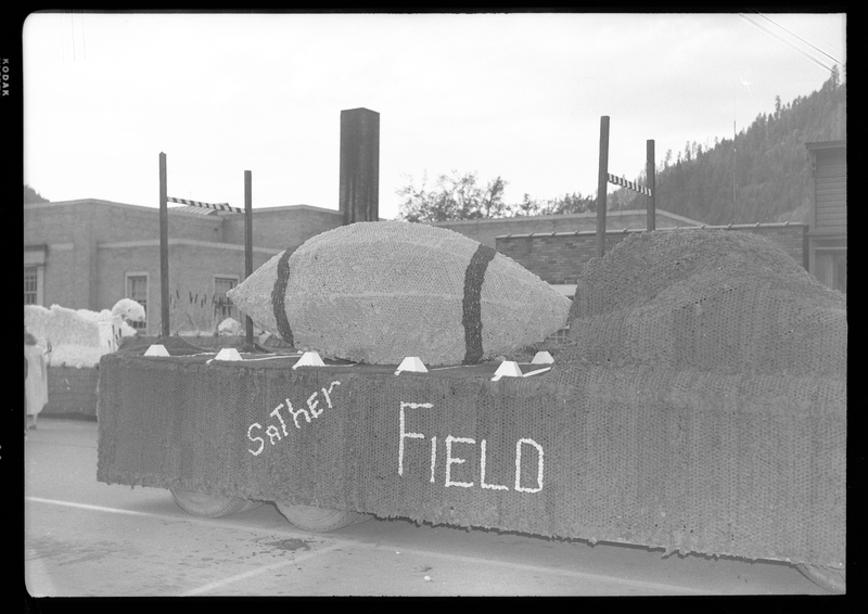 Sather field parade float for the Benevolent and Protective Order of Elks parade. The float is made to mimic a football field, with two goal posts and a giant football. The float is parked in front of a building.