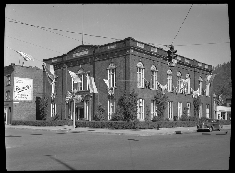 Photo of the building for the Benevolent and Protective Order of Elks taken across a corner street. Flags are hung across the street under the stop light, and there is a car in front of the building. 