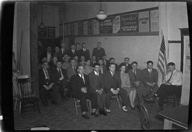 A group of mostly men and a few women gather for a union meeting. Most of the people are sitting in rows of chairs, and a few men stand in the back. Everyone is looking to the camera for the photo.