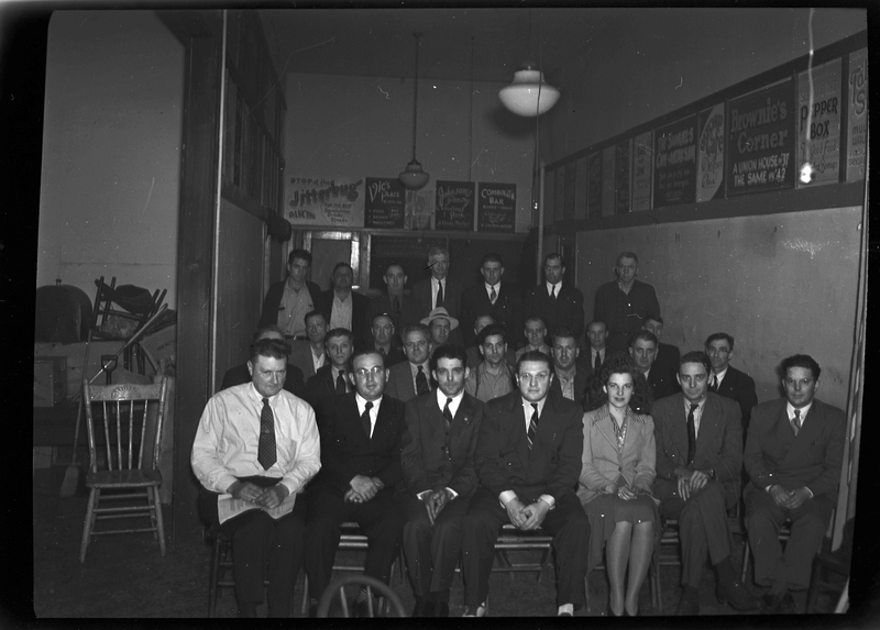 A group of mostly men and a few women gather for a union meeting. Most of the people are sitting in rows of chairs, and a few men stand in the back. Everyone is looking to the camera for the photo.