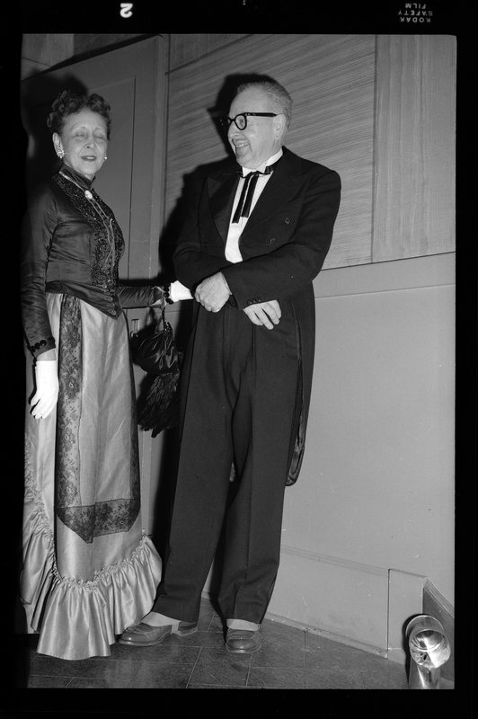 An older man and woman are standing together at a Rotary Club party. They are both formally dressed and the man is smiling at the woman.