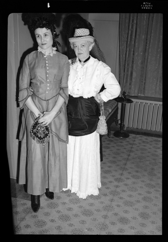 Two women in dresses at a Rotary Club party. One woman is looking at the camera and the other is looking behind it.