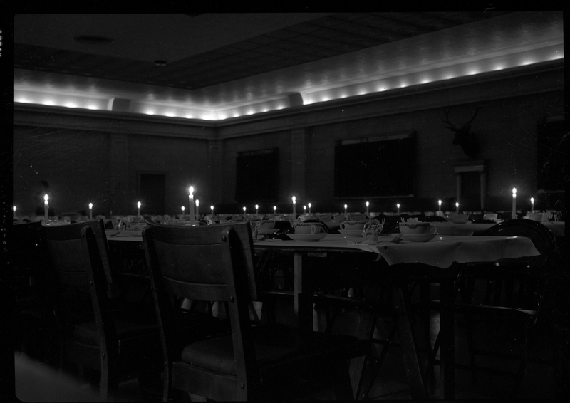 Photo of empty tables at a Rotary Club party. They have dishes and lit candles on them, but no people are visible.