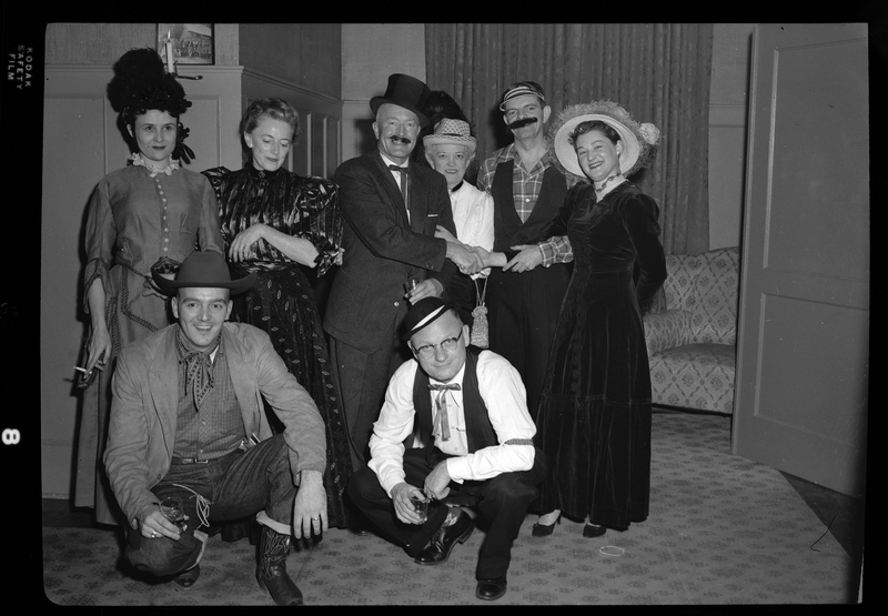 A group of men and women pose together for a photo. Most people are dressed up but some are in costumes. Most of them are looking at and/or smiling for the camera.