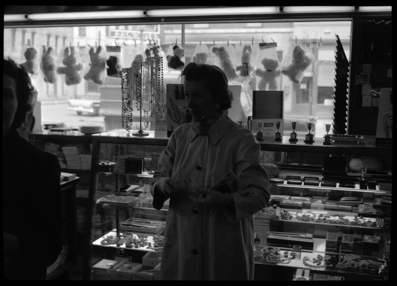 Photo of a woman at a Rotary Club party or possibly inside the Tabor store. She is well dressed and looking off into the distance. Behind her is a glass case holding various objects.