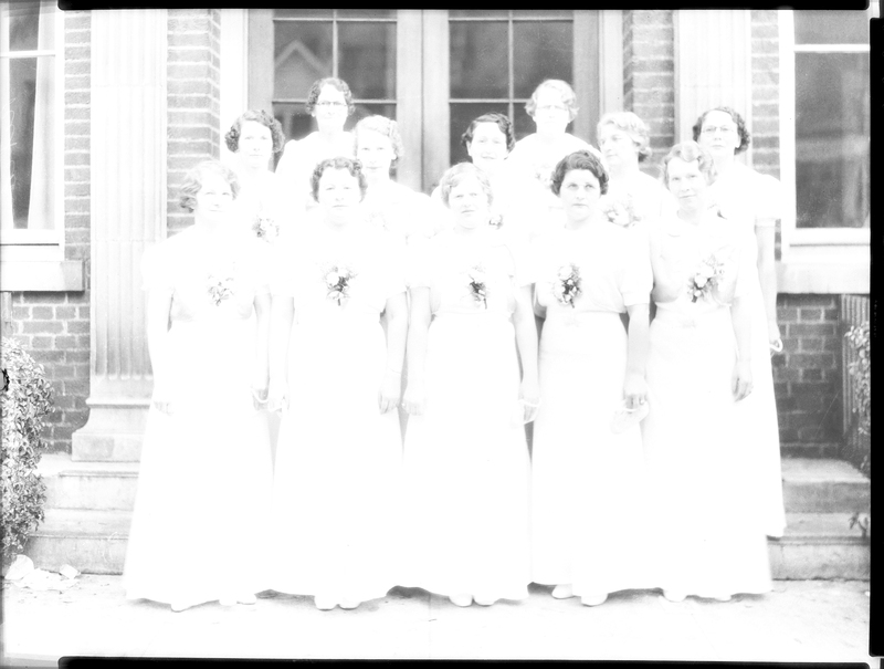 Overexposed photo of women standing together, previously described as "Rebecca's Degree Team." The shape of a few people's heads can be made out, as well as the brick of a building, but the photo is almost completely washed out. The women appear to be wearing matching dresses.