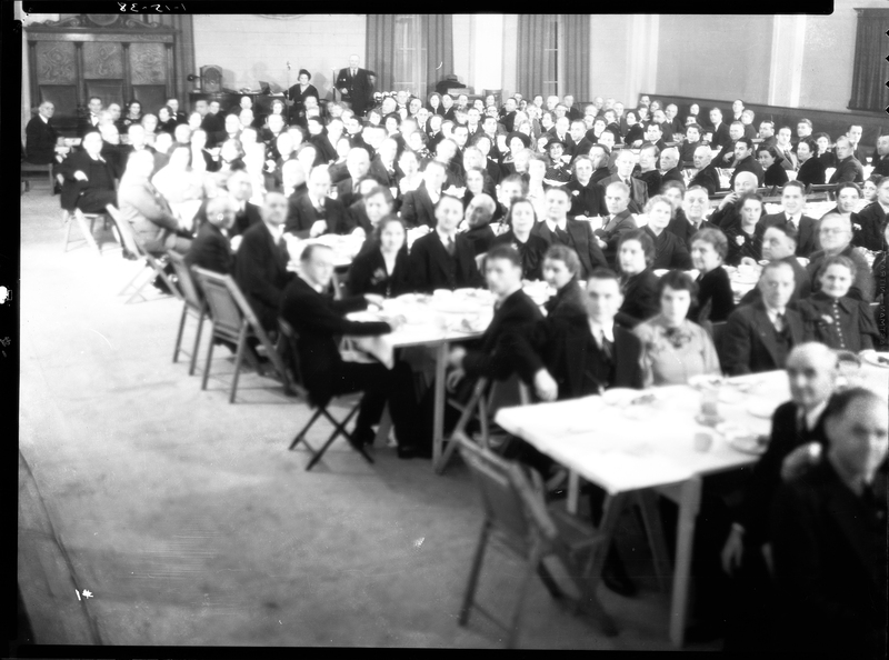 A large crowd of people seated at tables for an event by the Benevolent and Protective Order of Elks, likely the Burning Mortgage and Banquet. Some of the people's faces are washed out, but it looks as if everyone is looking at the camera for the photo.