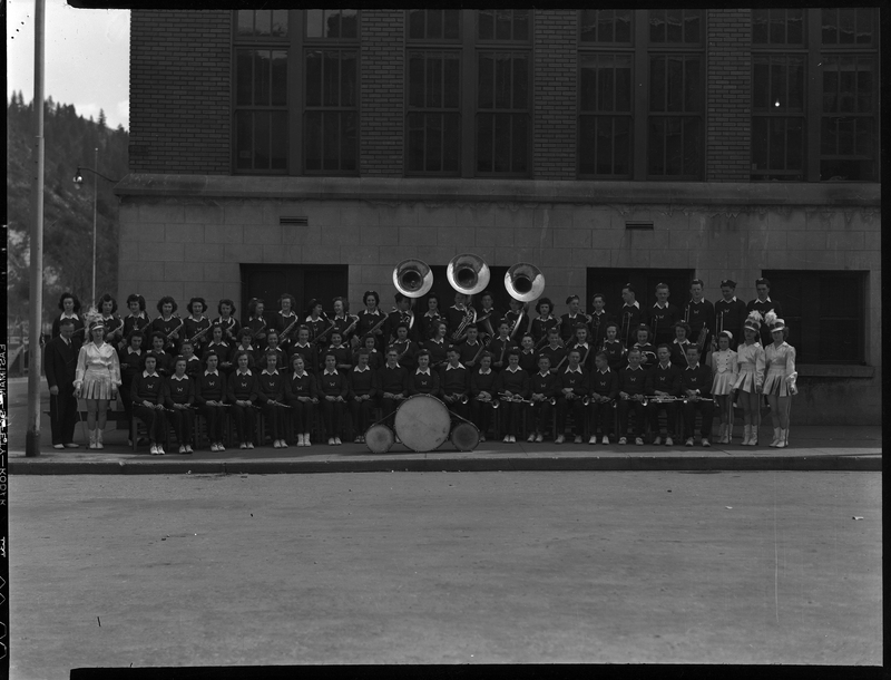 Wallace High School band members standing together for photo with their instruments. They are standing outside in front of buildings and everyone is wearing their uniforms.