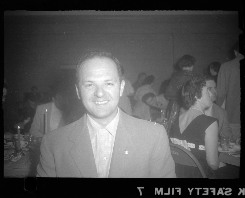 Photo of an unidentified man smiling for the camera at a Rotary Party. There are people visible in the background.