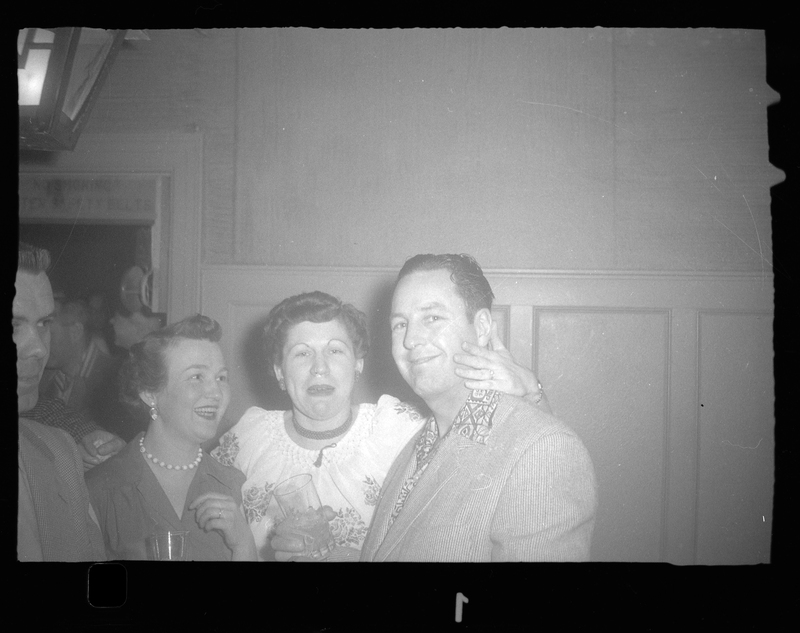 Two women and a man at Rotary Party. One of the women is touching the man's face as they pose for a photo. The women are holding drinks.