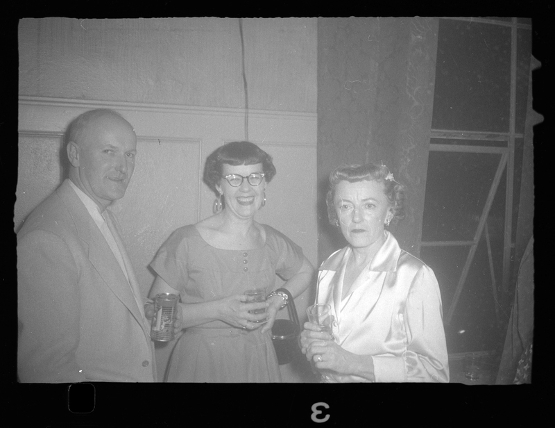 Two women and a man stand together at a Rotary Party. They are all holding drinks and one of the women and the man are smiling at the camera.