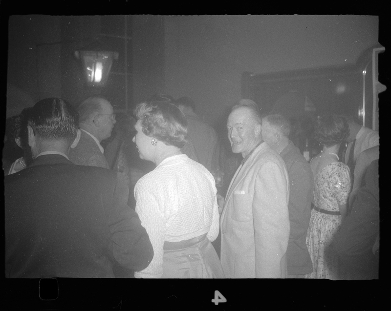 Photo of people at Rotary Party. All but one man are looking and/or facing away from the camera. The man looking at the camera is smiling.
