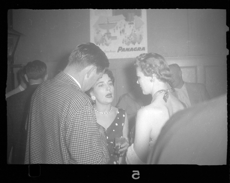 Two women and a man standing together and talking at Rotary Party. One woman and the man have their backs to the camera, and the other woman is looking at them. 