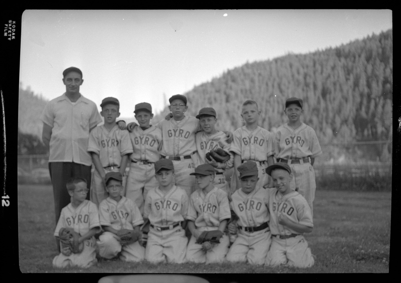 Group photo of the Gyro Little League baseball team and their coach. Front Row, from left to right: (twins) Dick & Charles Vester; Roger Branz, (unknown), Dave Featherstone & David Albertini. Back Row: Coach Bill English, Gary Prolo, (unknown), Jim McHeffey, (unknown), (unknown) & Billy Pat English (son of the Coach). They are wearing matching uniforms and a few are holding baseball gloves.