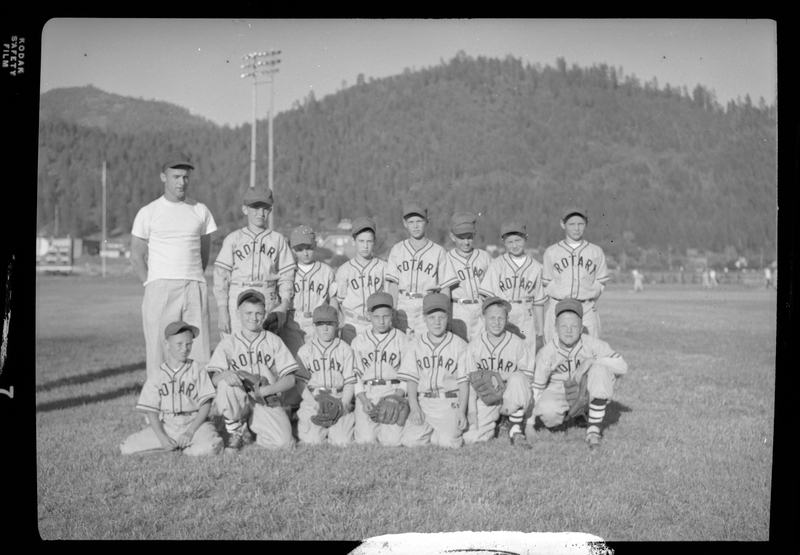 Group photo of the Rotary Little League baseball team and their coach. Front Row, from left to right: (unknown), (unknown), (unknown), Tom Mohr, (unknown), (unknown) & Pat Wheeler. Back Row: Coach Bud Riley, Dennis Wheeler, (unknown), Robbie Fairweather, (unknown), (unknown), (unknown), (unknown). They are wearing matching uniforms and a few are holding baseball gloves.