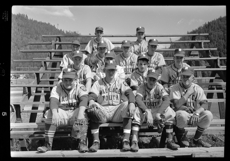 Group photo of the Wallace Youth Baseball team. The team are seated in rows on bleachers, wearing their uniforms and gloves. Previously described as "Legion baseball team all-stars."