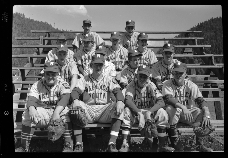 Group photo of the Wallace American Legion All Star Team at Sather Field, Silverton, ID. The team members are seated in rows on bleachers, wearing their uniforms and gloves. Front Row, from left to right:  Paul Mollendorf, Bob Sands, (unknown), (unknown). 2nd Row:  Dave Keller, (unknown), Mike Foreman & Chuck Keiffer. 3rd Row: Pete Zanetti, John Bardelli, Dan Malcolm & Larry MacGuffie. Back Row: Billy Pat English & Paul Murray. This photograph was previously described as "Legion baseball team all-stars."