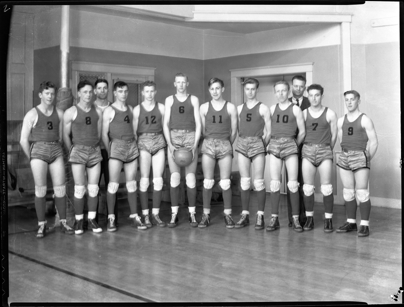 Photo of the Wallace High School Basketball team lined up with their coaches standing behind them. They are wearing matching uniforms and the man in the middle of the line is holding a basketball.