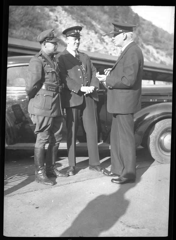 Three police officers in uniform stand in front of a car. Previously described as "Tom Barrett, Vic Langley, and Charles Pugh. Police photographs."