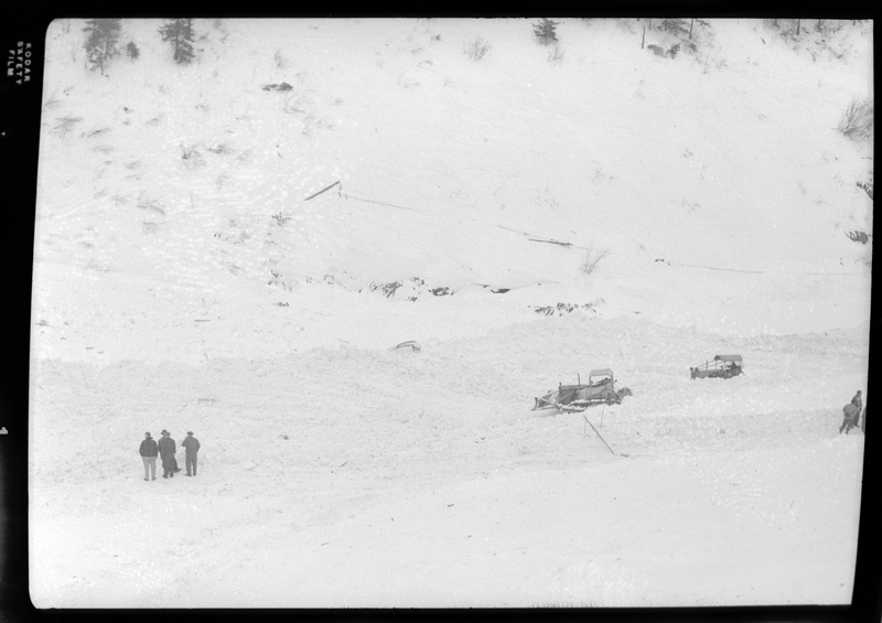 Photo of the aftermath of an avalanche in Burke, Idaho. A group of men can be seen in the snow on the left, and there are a few vehicles, presumably to clear away the snow, off to the side.