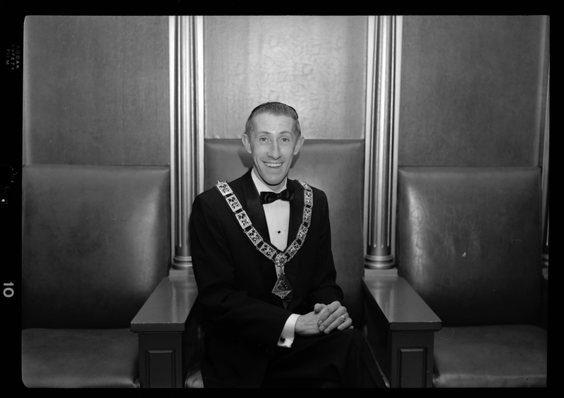Photo of the Exalted Ruler of the Benevolent and Protective Order of Elks, Bob Wheeler. He is sitting in a chair, wearing a tuxedo, and a pendant.