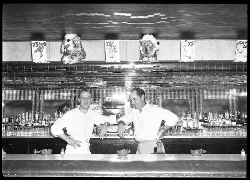 Harold Rullman and Babe Streeter, partners, standing in Sweet's Bar. They are standing next to each other behind the bar and leaning against the cash register.