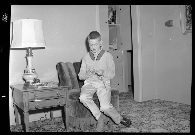 Photo of Les Randall's son who is sitting on a chair and holding what is probably a fishing line.