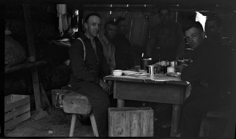 Two unidentified men are sitting at a table inside a cabin eating.