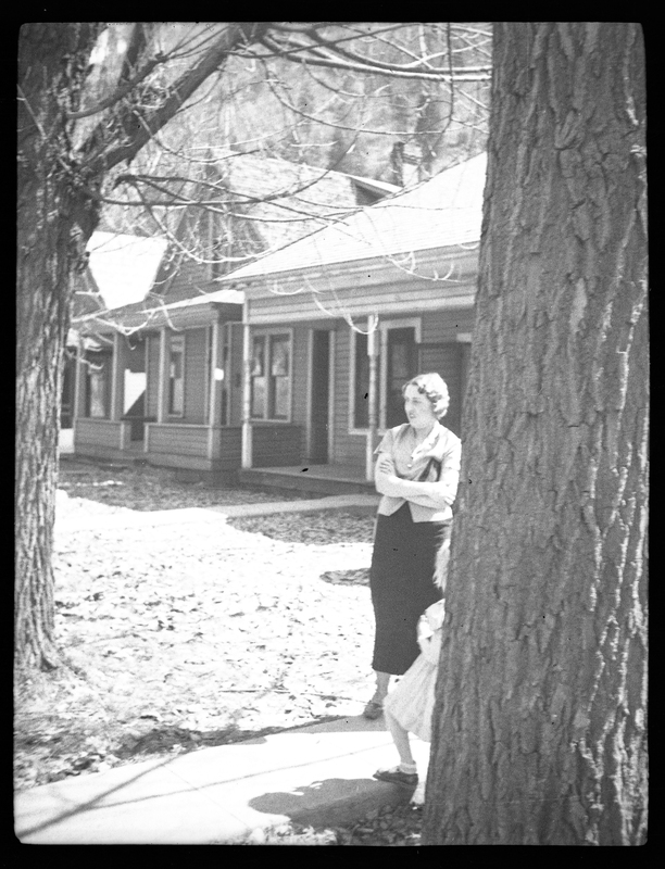 Photo of a woman standing next to a tree. There are houses in the background.