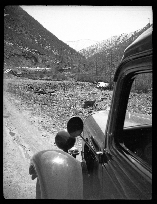 Photo taken close to the side of a car, where part of it is visible. The subject of the photo appears to be the landscape in front of the car, which is mostly bare trees and a steep hill, possibly a mountain.