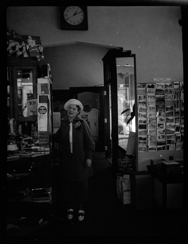 Photo of an unidentified woman standing inside of a store, presumably shopping. She is wearing a beret and looking at the camera.
