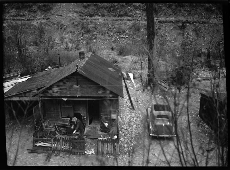 Photo of a man inspecting the damage done to Peter Paulson's home after a rock slide near Big Creek, Idaho. There is a car next to the damaged house.