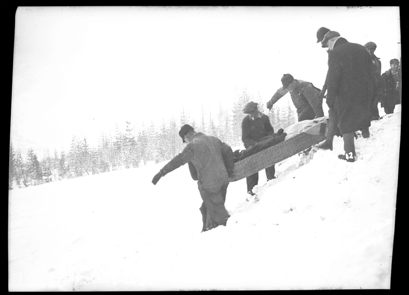 A group of people carrying someone on a stretcher down a snowy hill after an avalanche hit a train on Northern Pacific Railroad. Three people died.