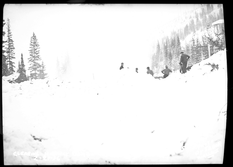 A few people can be seen standing behind a large pile of snow after an avalanche hit a train on the Northern Pacific Railroad. Three people died.