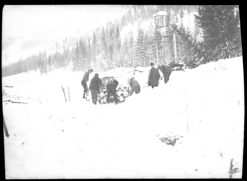 A group of people stand around in the snow, hunched over and examining something after an avalanche hit a train on the Northern Pacific Railroad. Three people died.