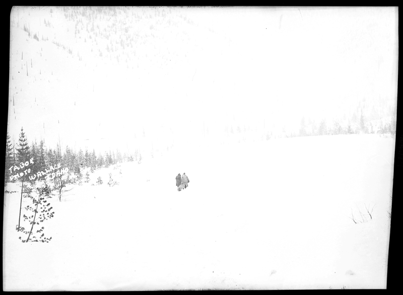 Two people can be seen walking through the heavy snow after an avalanche hit a train on the Northern Pacific Railroad. Most of the photo is overexposed, but the people appear to be dragging something behind them. Photos say that three people died.