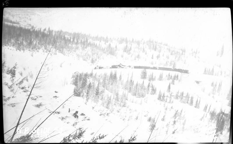 Photo of the entire train in the distance after an avalanche hit it on Northern Pacific Railroad on Highway U.S. 10 near Wallace, Idaho. Photos say that three people died. The path of the avalanche is visible from the knocked down trees.