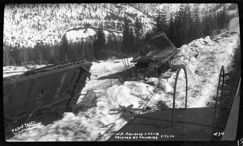 Photo of a train coach that was crushed as a result of an avalanche that hit a train on the Northern Pacific Railroad. The coach car was forced off of the tracks, and is completely destroyed after it was split in two pieces. Other photos say that three people died.