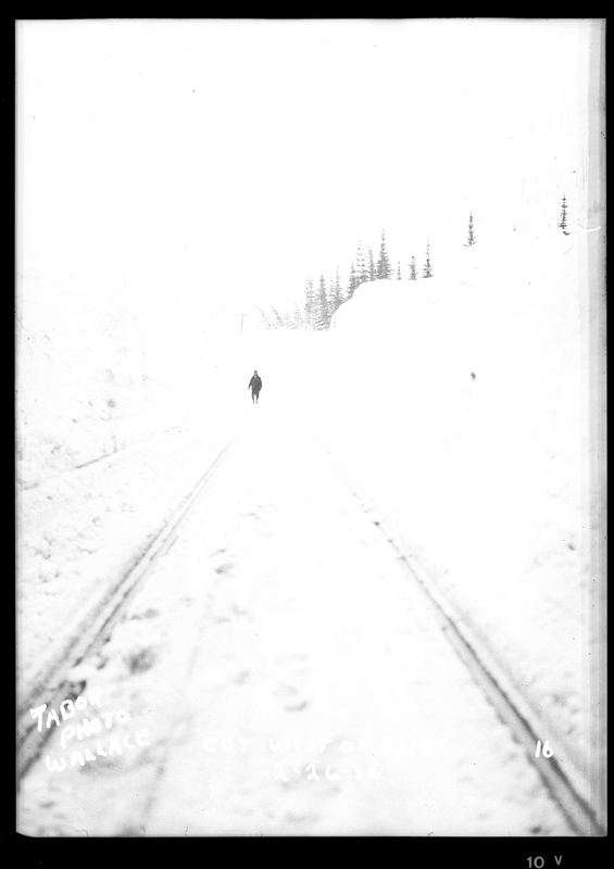 An unidentified person is walking on the snow covered train tracks, presumably after an avalanche. The photo is overexposed. Text on photo reads: "Cut West of Slide."