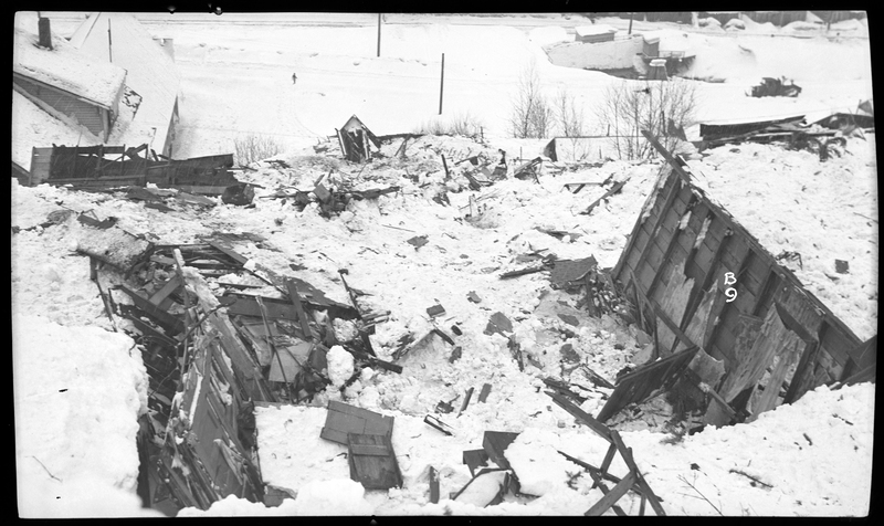Photo of the damage caused by an avalanche in Burke, Idaho. The damage appears to have been done to buildings, and the area is covered in debris and snow.