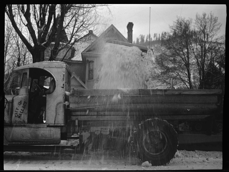 Photo of the side of a snow loading truck in Wallace, Idaho that is actively picking up snow from the street. The driver side door has "City of Wallace" written on it.