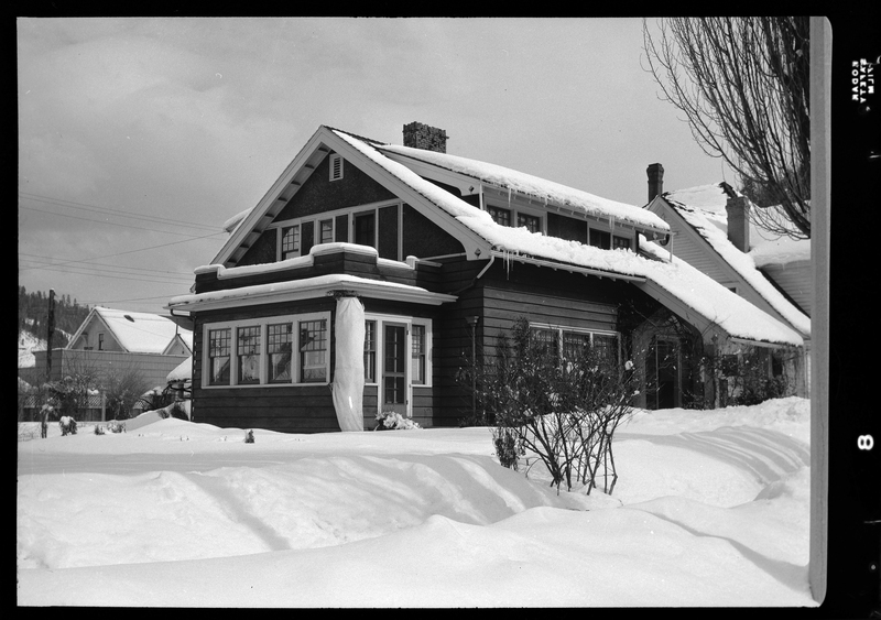 Photo of a snow covered house. There is snow on the roof, and several inches of snow on the ground around the house.