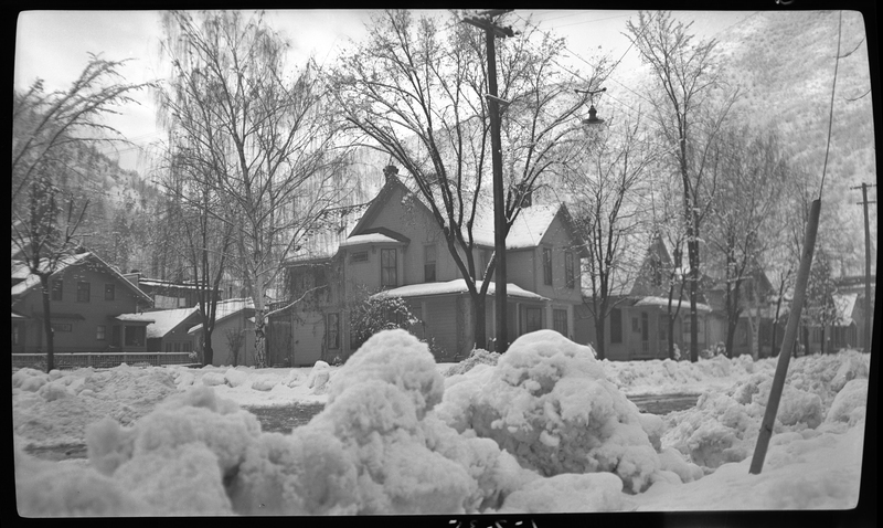 Photo of several houses in the snow in Wallace, Idaho. 224 Cedar Street, at the intersection of Cedar and Third Streets, is in the foreground. The trees and sidewalks are covered in snow, but the streets appear to be plowed.