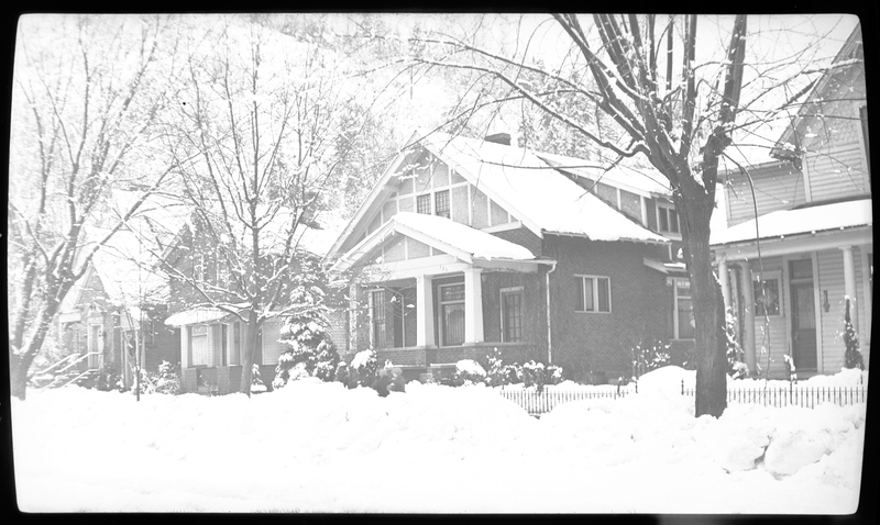 Photo of four houses in Wallace, Idaho, possibly on Pine Street or King Street, in the snow. The trees around the houses are also covered in snow, as is the ground.