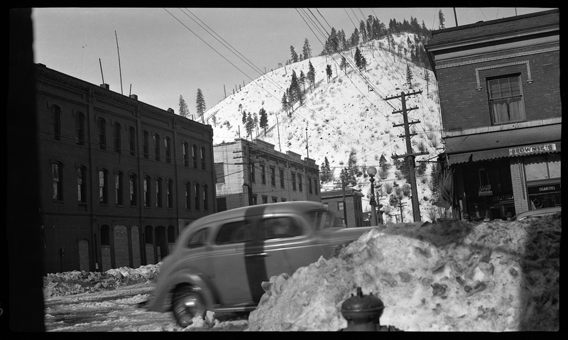 Photo of a car parked on a snowy covered street that is surrounded by buildings in Wallace, Idaho.